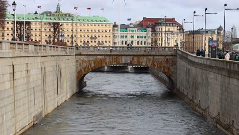 Stone-bridge-over-water-by-Grand-Hotel-in-Stockholm-on-cloudy-day,-slo-mo