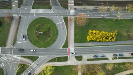 Aerial---traffic-roundabout-with-pedestrian-crossings-and-vehicles,-surrounded-by-green-spaces-and-trees