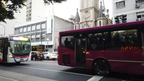 Bus-car-taxi-traffic-at-public-transport-rivadavia-avenue-church-background-latin-city-traffic,-Lourdes-Church-background