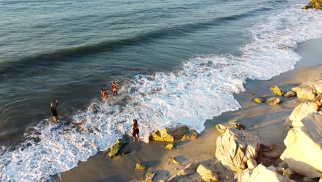 Gente-Disfrutando-De-Un-Día-Soleado-En-Una-Playa-Rocosa,-Olas-Rompiendo-Suavemente,-Vista-Aérea