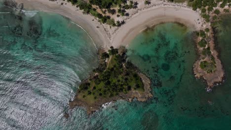 Aerial-rotating-birdseye-view-of-curved-sandy-beaches-along-a-rocky-tropical-coast-with-waves-and-coral-reefs