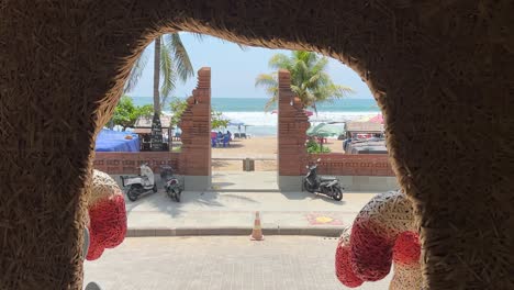 Looking-through-beach-resort-archway-to-Legian-Beach-in-Bali,-Indonesia-with-motorbikes-going-by