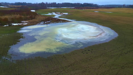 Aerial-panning-view-of-Latvian-landscape,-frozen-leakage-from-deciduous-forest