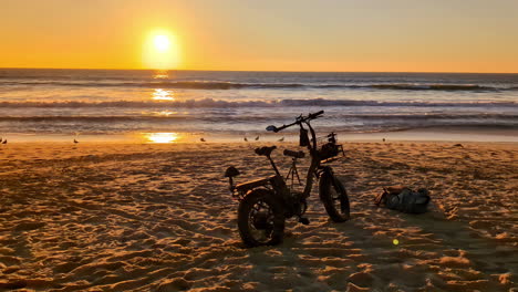 Bicicleta-Eléctrica-En-La-Playa-Con-Puesta-De-Sol-Al-Fondo-Sobre-El-Mar.