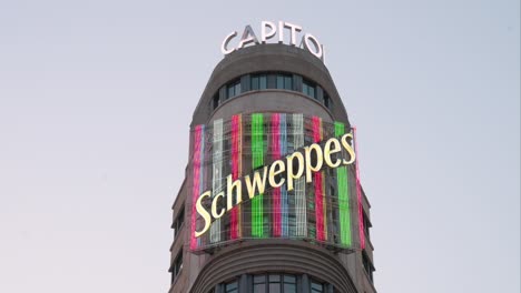 Ein-Lebendiges,-Farbenfrohes-Neonschild-Von-Schweppes-Schmückt-Das-Aas-Gebäude,-Bekannt-Als-Das-Capitol,-An-Der-Gran-Via-In-Madrid,-Einem-Geschäftigen-Zentrum-Für-Abendliche-Unterhaltung-Und-Einzelhandel