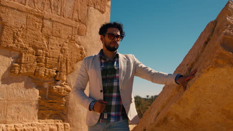 Hispanic-male-tourist-standing-in-front-of-Egyptian-hieroglyphs-carved-red-wall-in-Ancient-Egypt