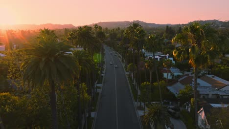 Slow-and-Calm-Drone-Establishing-Shot,-Birds-Eye-View-of-Historical-Beverly-Hills-Neighborhood-at-Golden-Hour,-Cars-on-Tree-Lined-Street-with-Warm-Sun-Hitting-Luxury-Residences