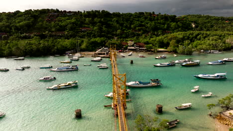 Kultige-Gelbe-Brücke,-Die-Die-Inseln-Nusa-Lembongan-Und-Nusa-Ceningan-Auf-Bali-Verbindet,-Mit-Booten,-Die-Im-Türkisfarbenen-Meerwasser-Festgemacht-Sind