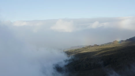 Vista-Aérea-De-Las-Nubes-Sobre-Las-Laderas-De-Las-Montañas-Con-Un-Arco-Iris-Claro-En-El-Volcán-Haleakala