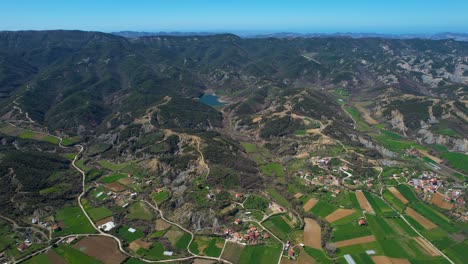 Pueblo-Pintoresco-En-La-Ladera-De-Una-Colina:-Casas-Encantadoras,-Parcelas-Verdes,-Invernaderos-Y-Agricultura-Primaveral-Que-Florece-En-Un-Hermoso-Valle-En-Albania