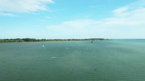 Eine-Luftaufnahme-Von-Mehreren-Kitesurfern-In-Der-Ferne,-Die-An-Einem-Windigen-Spätsommertag-Schnell-Auf-Dem-Wasser-Der-Donau-Segeln