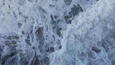 Drone-shot-straight-down-of-ocean-waves-washing-around-during-high-tide