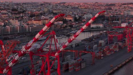 Tele-Nahaufnahme-Aus-Der-Luft-Von-Roten-Und-Weißen-Containerkränen-Im-Hafen-An-Land-Und-Der-Stadtkulisse