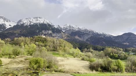 Blick-Aus-Dem-Zugfenster-Auf-Majestätische-Schneebedeckte-Berge,-Die-über-üppigen-Grünen-Tälern-Aufragen