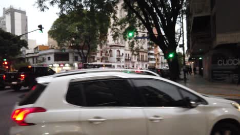Cars-turning-right-the-street-at-alberdi-avenue,-dusk-skyline-traffic-in-buenos-aires-city-argentina-pedestrians-and-neighborhood-buildings-of-flores