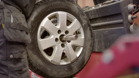 Tyre-technician-places-car-wheel-on-wheel-balancer-to-rebalance-after-repair