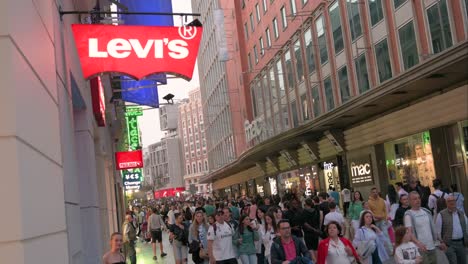 Pedestrians-and-shoppers-walk-past-the-American-clothing-company-brand,-Levi's-store-and-logo-sign-on-a-commercial-retail-street-at-night