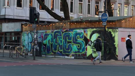 Pedestrians-walk-by-vibrant-street-art-in-Manchester's-Northern-Quarter,-evening-light