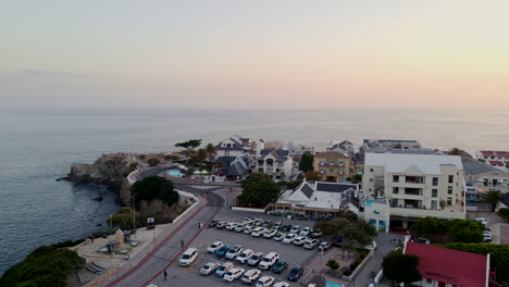 Vista-Panorámica-De-Drones-Sobre-El-Antiguo-Puerto-Y-El-Pueblo-Costero-Turístico-De-Hermanus-Al-Atardecer