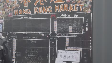 Cámara-Lenta-De-Personas-Caminando-Frente-A-Un-Mapa-Del-Mercado-De-Hong-Kong-En-Las-Barras