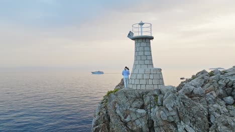 Kalamota-Island,-Adriatic-Sea,-Croatia---A-Couple-Relishing-the-Sunset-Beside-the-Lighthouse---Orbit-Drone-Shot