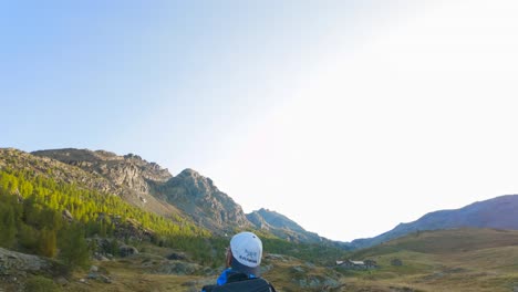 Inclínese-Hacia-Abajo-Desde-El-Cielo-Azul-Claro-Para-Revelar-Un-Excursionista-Masculino-Caminando-Por-El-Valle-De-La-Pradera-Salvaje-En-Los-Alpes-De-Valmalenco