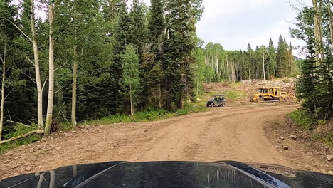 Passing-by-industrial-forest-cutting-machines,-driving-POV-on-gravel-road