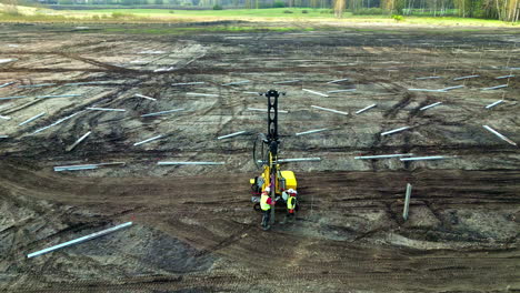 Aerial-drone-rotate-above-construction-workers-measuring-fields-industrial-tech-technology-people-wearing-safety-clothes-yellow-helmets,-machine-at-countryside-fields-panoramic