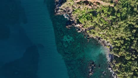 Wide-aerial-birdseye-view-of-a-rocky-tropical-coastline-with-lush-vegetation-on-steep-hills-and-cliffs