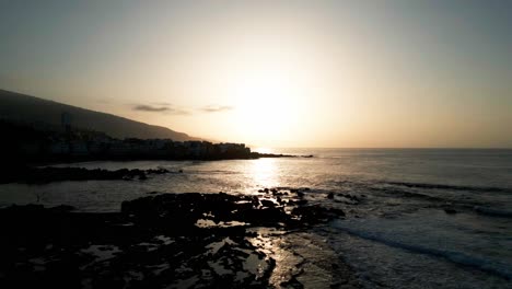 Drone-captures-the-Tenerife-coastline-at-dusk,-with-a-mesmerizing-blend-of-fading-light-and-tranquil-waves-meeting-the-shore