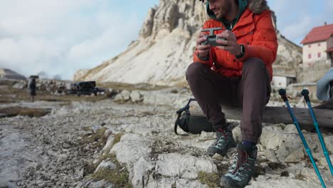 Seated-drone-pilot-operates-a-small-drone-while-hiking-in-the-Italian-Alps