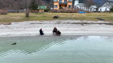 Mother-and-kids-play-in-cold-water-at-beach,-father-comes-into-frame-to-take-picture