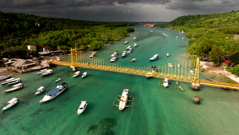 Bali,-Indonesien---Schiffe-Treiben-Auf-Dem-Meer-Mit-Der-Berühmten-Gelben-Brücke,-Die-Nusa-Lembongan-Und-Die-Insel-Ceningan-Im-Hintergrund-Verbindet---Luftaufnahme-Einer-Drohne