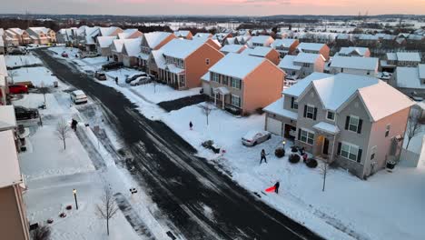 People-clearing-snow-and-children-playing-on-sleds-in-American-neighborhood-during-winter-sunset