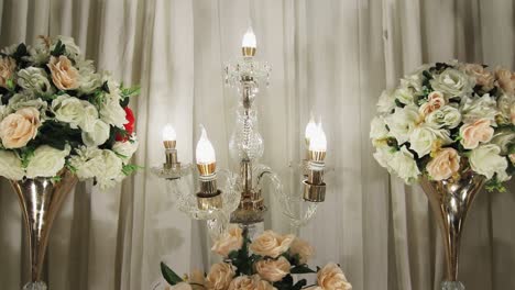 The-view-shows-a-close-up-of-a-decorative-piece-adorned-with-multiple-light-bulbs-and-flanked-by-two-lovely-bouquets-on-each-side