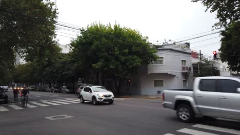 Automóviles-Circulando-Por-La-Avenida-Avellaneda-Flores-Tráfico-Del-Barrio-En-La-Ciudad-De-Buenos-Aires-Atardecer-Horizonte-árboles-Otoño,-Peatones-Y-Tiendas