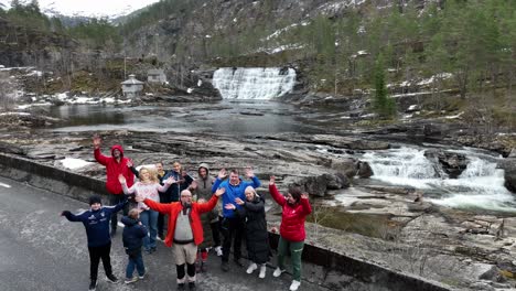 Feliz-Grupo-De-Turistas-Saludando-Y-Sonriendo-Frente-A-La-Cascada-De-Primavera-Durante-La-Visita-Guiada