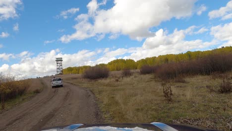 Weißer-Geländewagen-Fährt-Auf-Schotterstraße-In-Der-Nähe-Des-Aussichtsturms-Vorbei,-Front-POV-Aufnahme