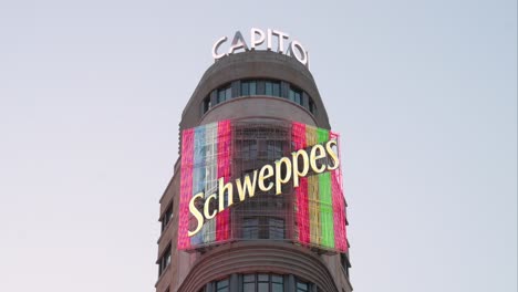 Un-Luminoso-Y-Colorido-Letrero-De-Neón-De-La-Marca-Suiza-De-Bebidas-Schweppes-Se-Ve-En-La-Fachada-Del-Edificio-Carroñero-De-Gran-Vía,-Conocido-Como-El-Capitolio.