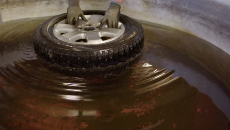 Placing-tyre-in-water-pool-of-workshop-to-locate-the-leak,-close-up