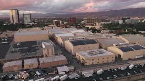 Aerial-Drone-Footage-of-WB-Studio-Lot-with-Dreamy-Pastel-Clouds-in-Sky-Above,-Grip-Trucks-Parked-by-Sound-Stages