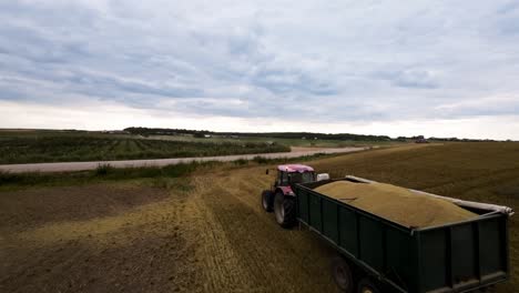 Seguimiento-De-Disparos-De-Drones,-Tractor-Con-Vagón-Que-Transporta-Trigo-Cosechado-Desde-El-Campo-Agrícola