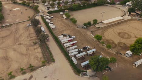 Aerial-Shot-of-LA-Equestrian-Center,-Trailers-and-Trucks-Moving-Slowly-Around-the-Lot,-Livery-Yards-with-Horses-and-Trainers-Below