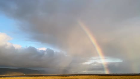 Rainbow-arching-over-cloudy-Icelandic-skies,-hint-of-sunlight,-serene-landscape