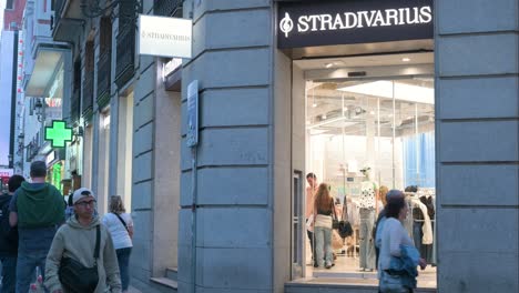 Compradores-Y-Peatones-Pasan-Por-La-Tienda-De-Moda-Española-De-Ropa-Femenina-De-España-Propiedad-Del-Grupo-Inditex,-Stradivarius,-Durante-La-Noche