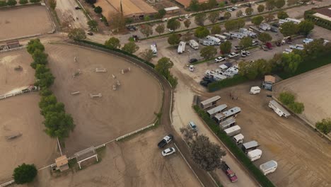 Aerial-Shot-of-Quaint-LA-Equestrian-Center-in-Burbank-at-Daytime,-Trucks-and-Trailers-Moving-Around-the-Lot,-Horses-Milling-About-in-Between-Pens