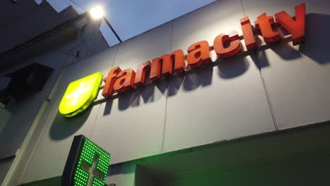 Farmacity-pharmacy-of-argentina-cross-green-sign-orange-letters-display-at-night-in-buenos-aires-city-entrance-closeup