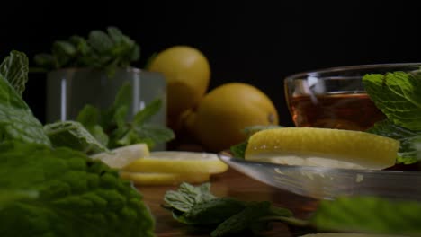 Close-up-dolly-of-fresh-lemon-balm,-and-tea-with-lemon-slices-on-table---commercial-shot