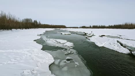 An-unfreezing-river-flows,-there-is-ice-along-the-banks