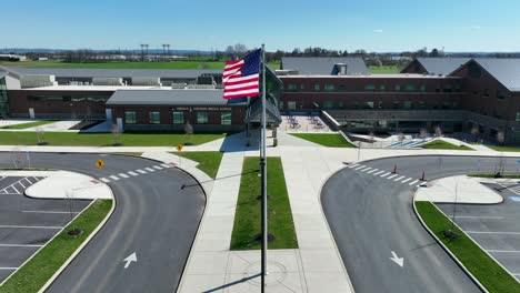 Toma-Aérea-Acercándose-A-La-Escuela-Del-Valle-De-Conestoga-Con-Bandera-Americana-En-Un-Día-Soleado